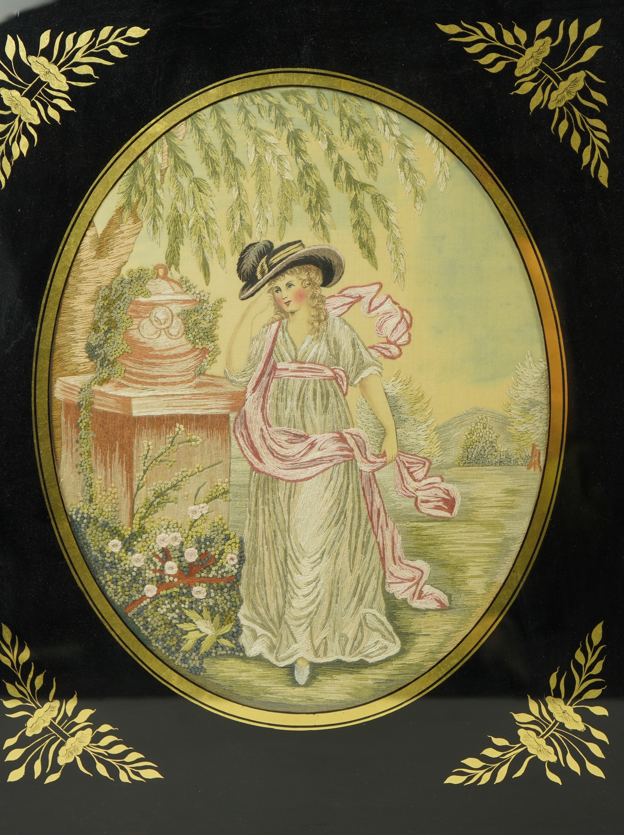 A pair of early 20th century oval silk embroideries of ladies standing by classical stone urns in a garden. Worked in pastel shades in silk using mostly stem stitch. Their faces, arms, hands and back ground silk hand pai